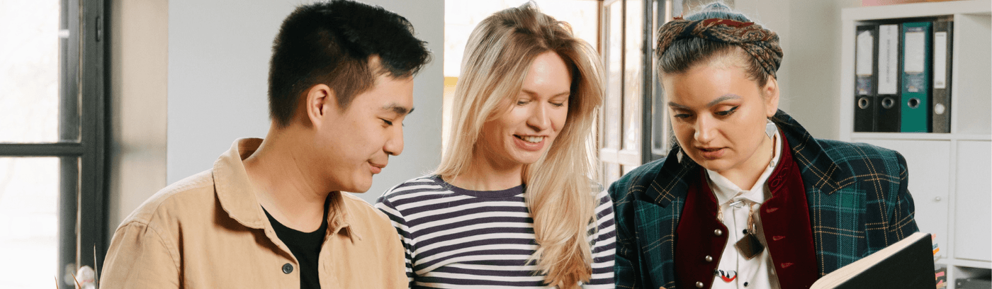Three people in an office reviewing documents together, engaged in discussion and collaboration.