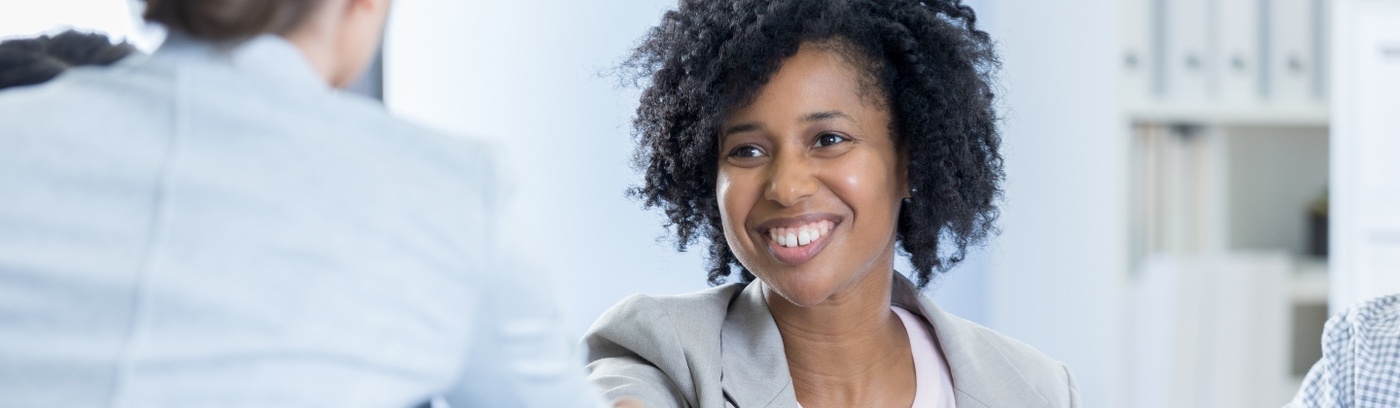 A woman engages in a handshake with two individuals during a professional meeting, symbolising collaboration and agreement.