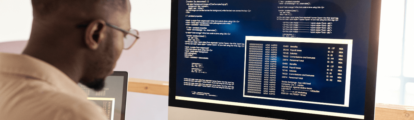 A man working intently at a computer, with a screen filled with programming code in front of him.