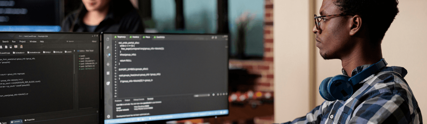 A man at a desk with two computer monitors and a keyboard, concentrating on cyber security work.
