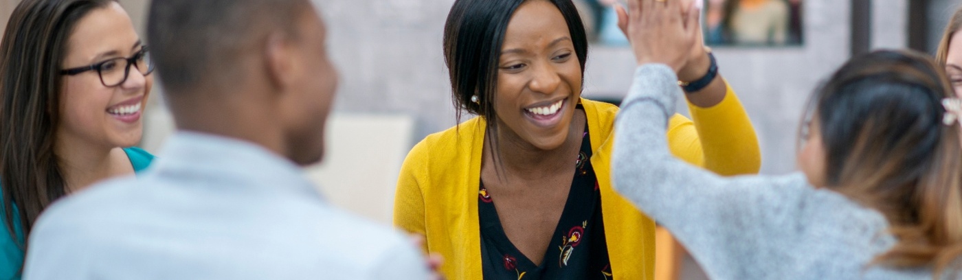 A lively scene of a woman giving a high five to a companion, surrounded by a group of people at a table, enjoying their time together.