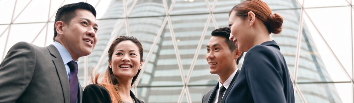 Three business professionals engaged in conversation outside a modern office building.