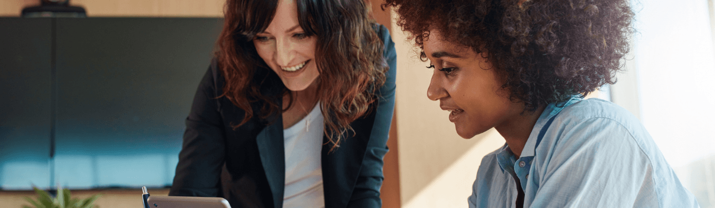 Two businesswomen attentively examining a tablet, engaged in discussion in a corporate environment.