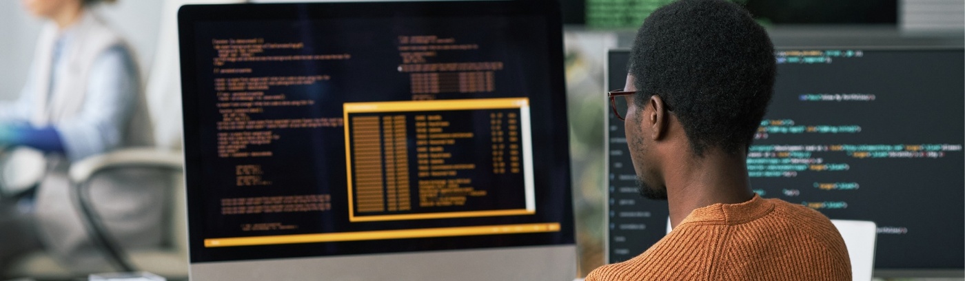 A man at a desk with dual monitors and a computer, engaged in work and surrounded by a productive environment.