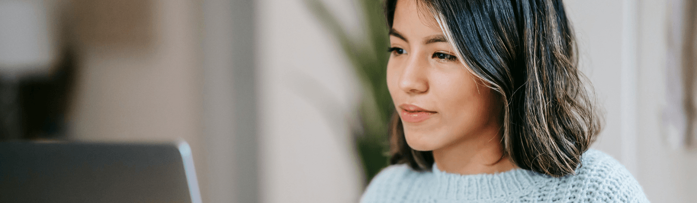 A woman working on a laptop at a table, appearing engaged and thoughtful in a cozy indoor setting.