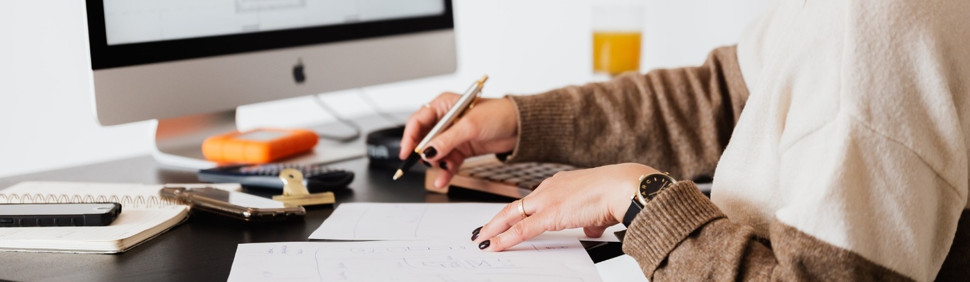 A woman sits at a desk, focused on her computer and sketching on a drawing pad, showcasing her creative workspace.