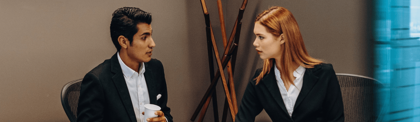 A man and woman in business attire engaged in a conversation in a professional setting.