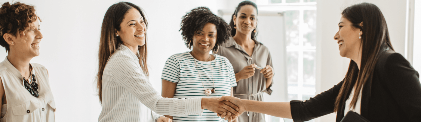 Women engaging in a handshake in an office meeting, representing partnership and professional interaction.