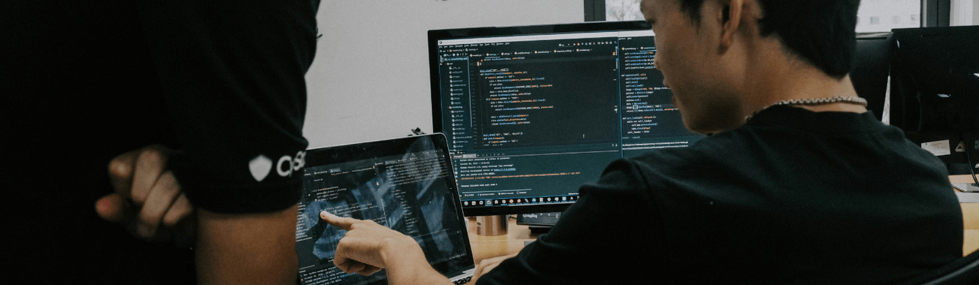 Two men engaged in work at a computer, looking at the monitor together.