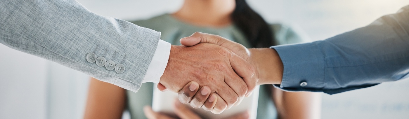 Two business individuals shaking hands in an office, representing a successful agreement or partnership in a professional environment.