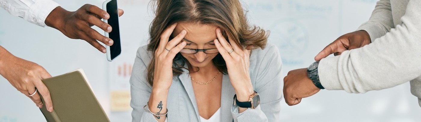 Surrounded by colleagues, a woman displays signs of distress, holding her head in her hands as they approach her with demands.