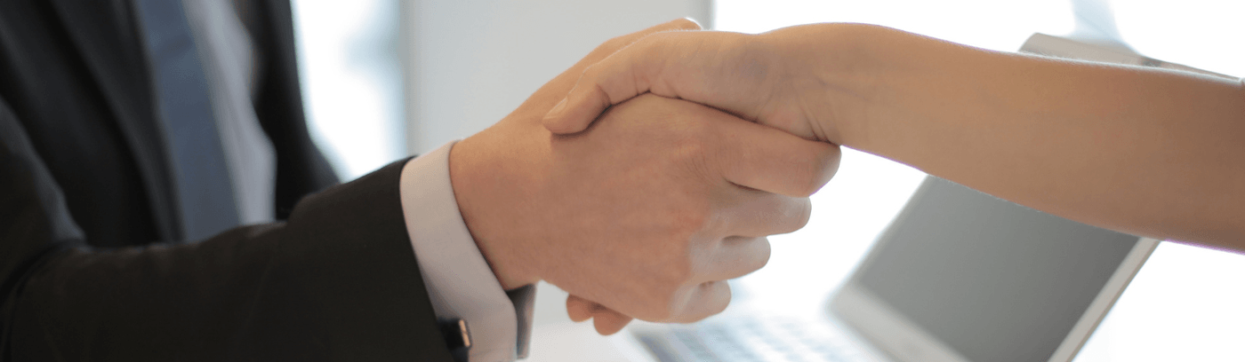 A person and another individual shaking hands in a professional setting, symbolising agreement or partnership.