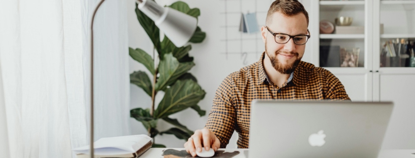 A man wearing glasses is seated at a desk, focused on his laptop while working diligently.