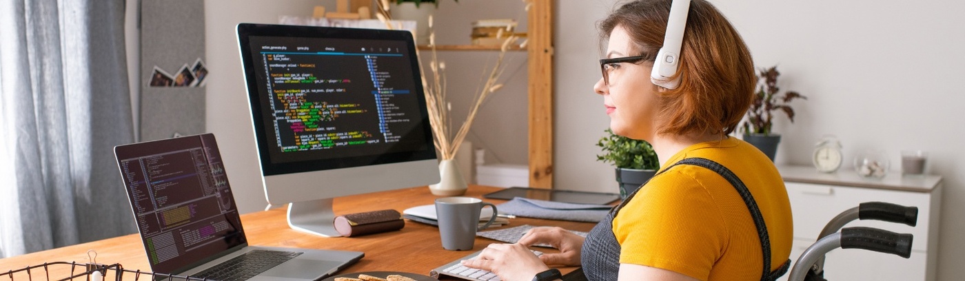 A woman in a wheelchair sits at a desk, actively working on a computer, showcasing her determination.