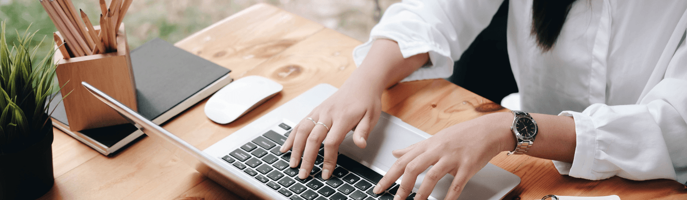 A woman engaged in typing on her laptop at a desk, with a notepad and pen visible nearby.