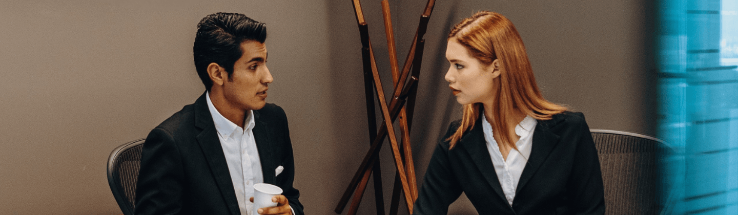 A man and woman in business attire engaged in a conversation in a professional setting.