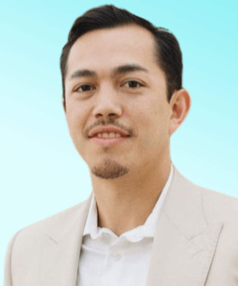 Man with dark hair in beige suit in front on light blue background