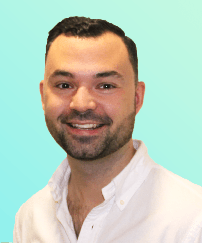 Man with short dark hair and stubble in a white shirt in front on mint green background smiling