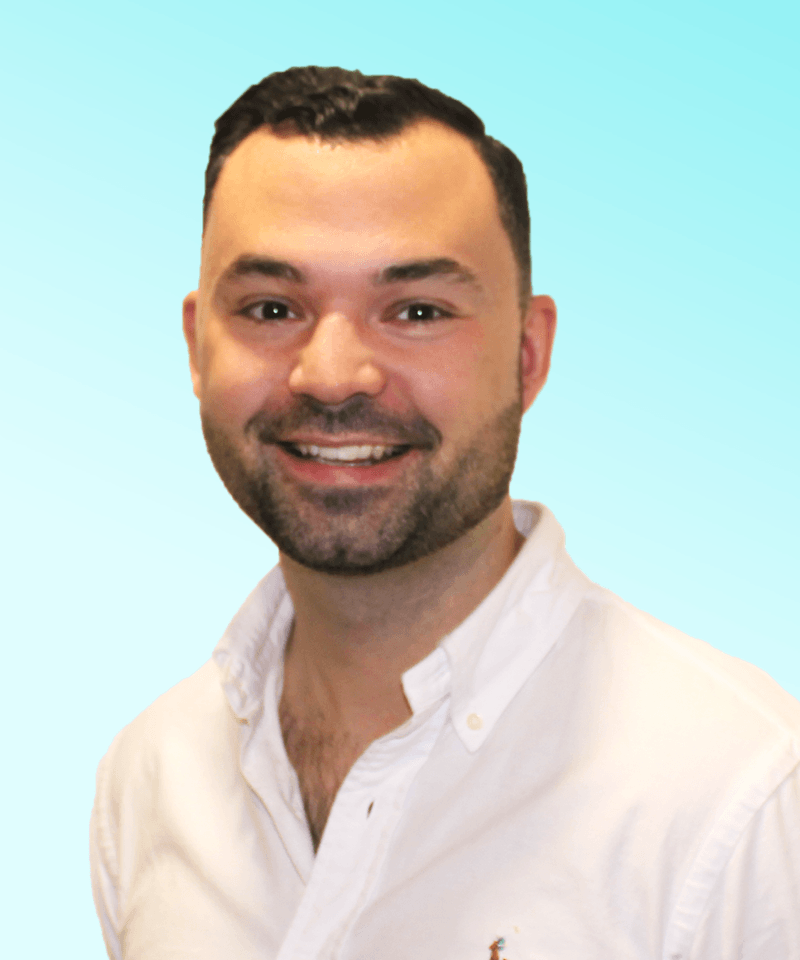 Man with short dark hair and stubble in a white shirt in front on blue background smiling