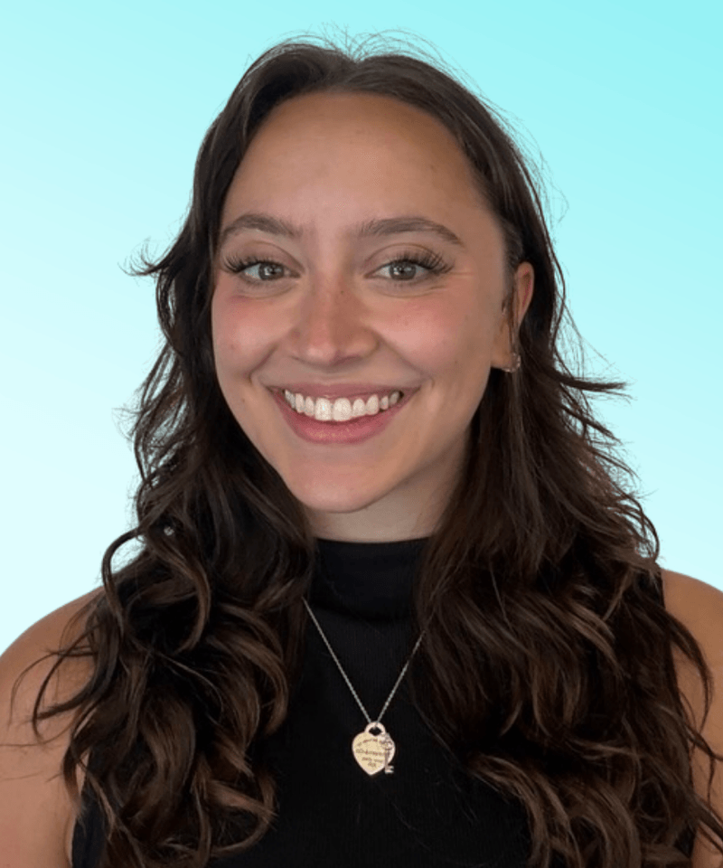Woman with brown hair and a black top smiling in front of blue background