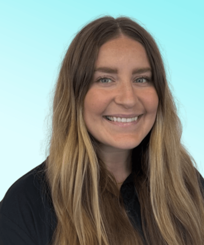 Woman with brunette hair and blonde highlights in a black shirt in front of blue background