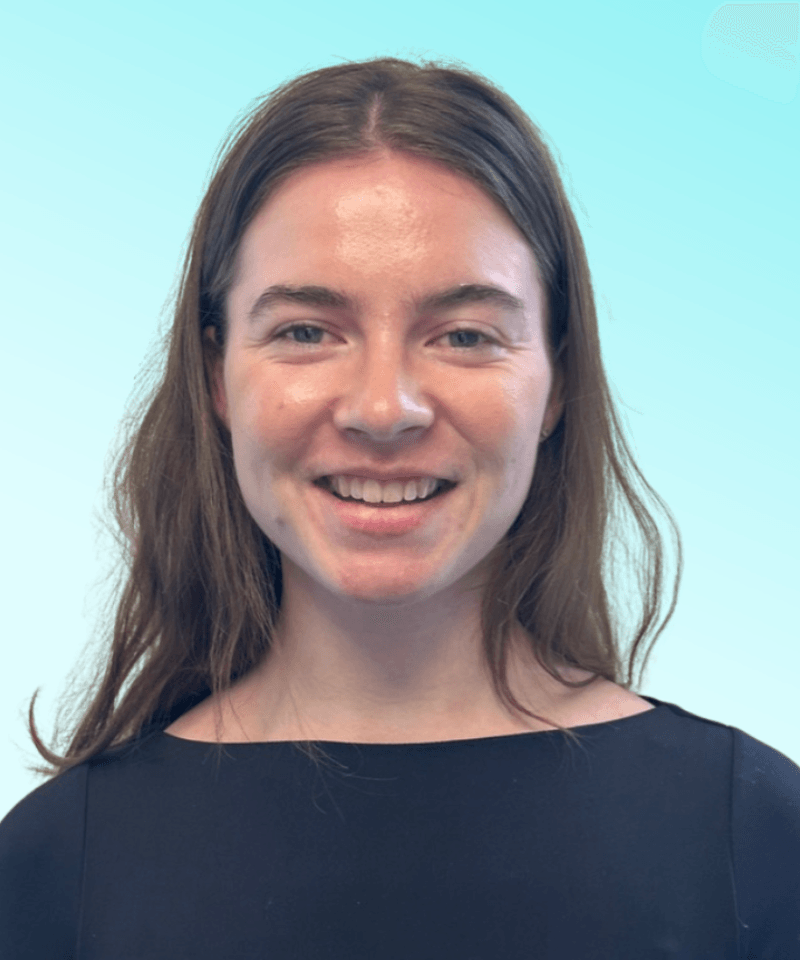 Woman with brunette hair and a black blouse smiling in front of blue background