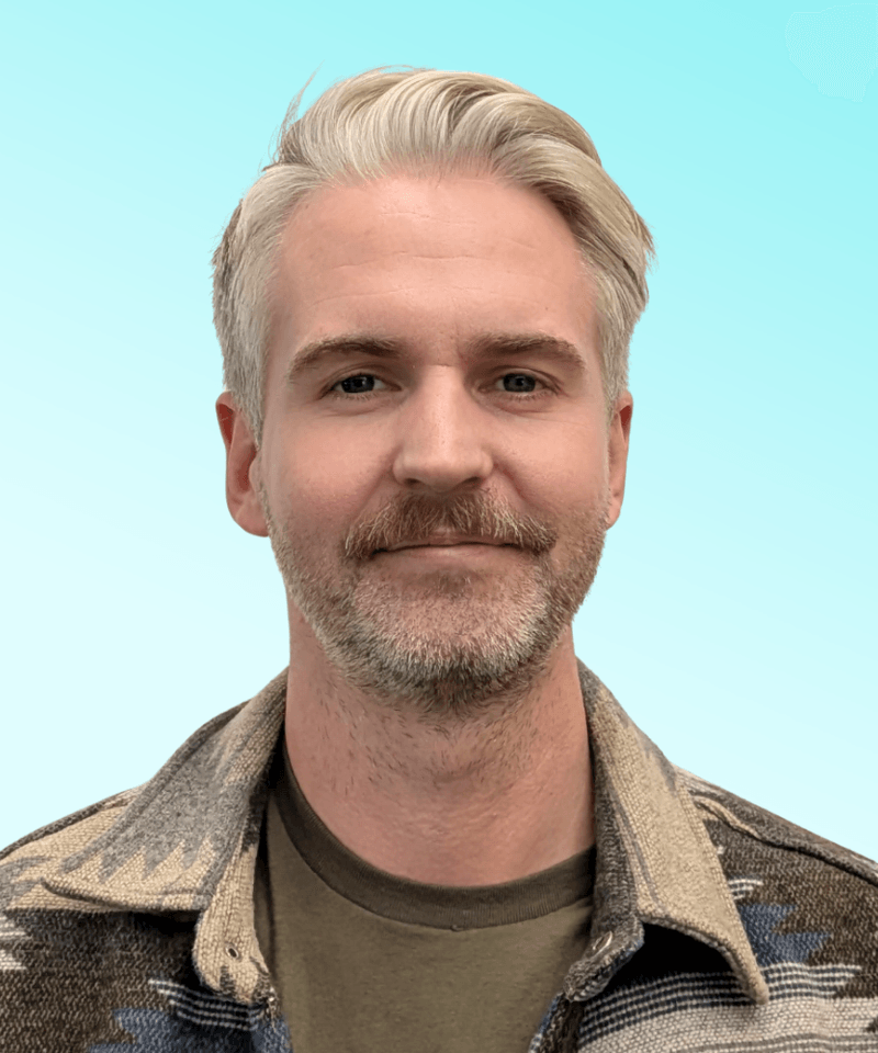 Man with grey hair and stubble with mustache in front of blue background