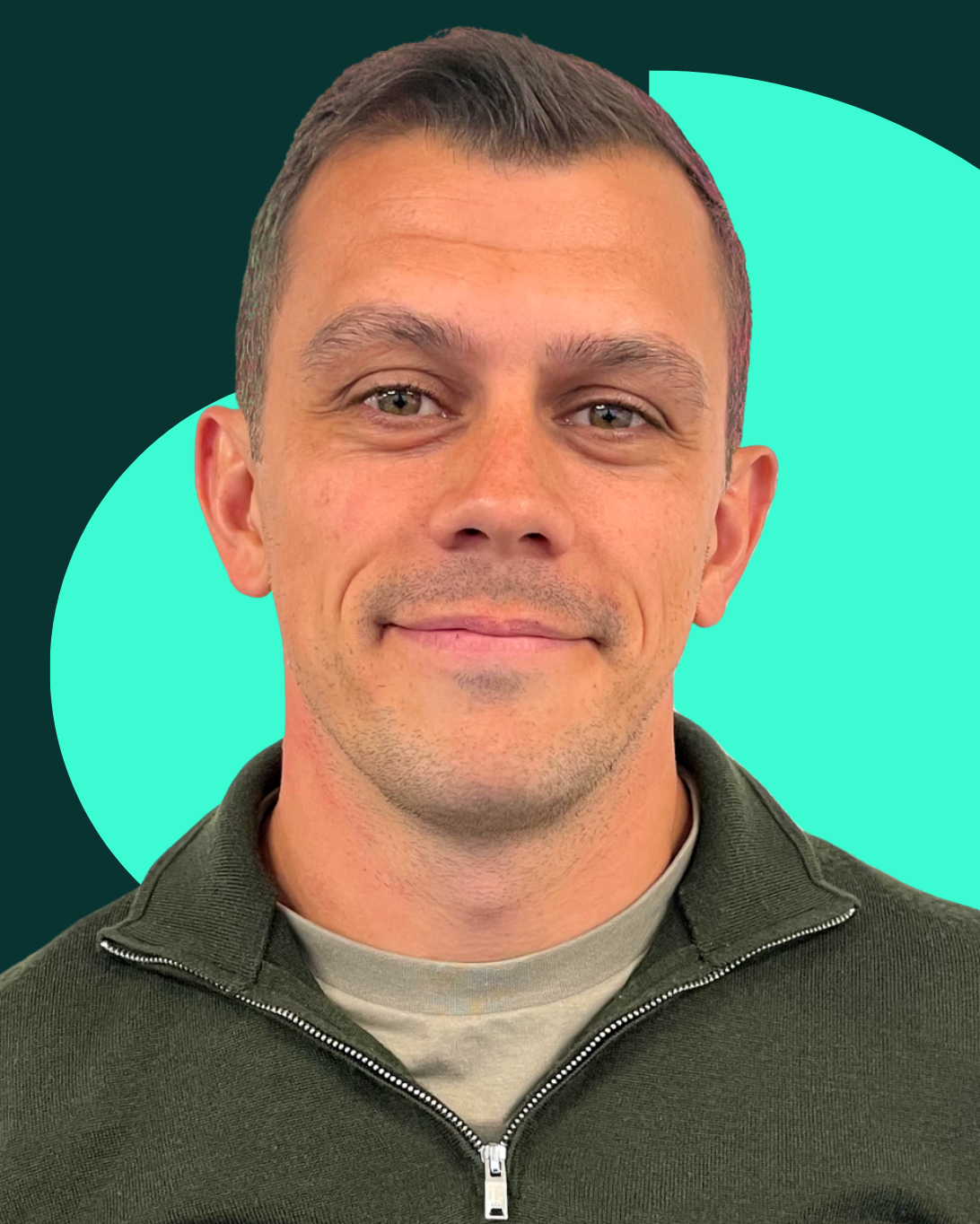Myles Jackson smiling, wearing a green zip-up sweater, in front of a red geometric pattern.
