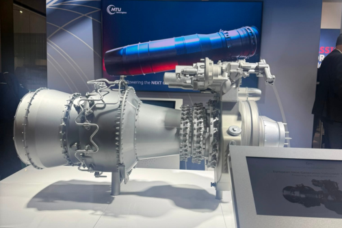 A detailed aircraft engine demonstrator displayed at an aerospace exhibition, showcasing advanced propulsion technology alongside a digital presentation and an aircraft model suspended overhead.